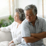 Upset couple sitting on a couch, woman looking ahead, man with crossed arms; concept is apology