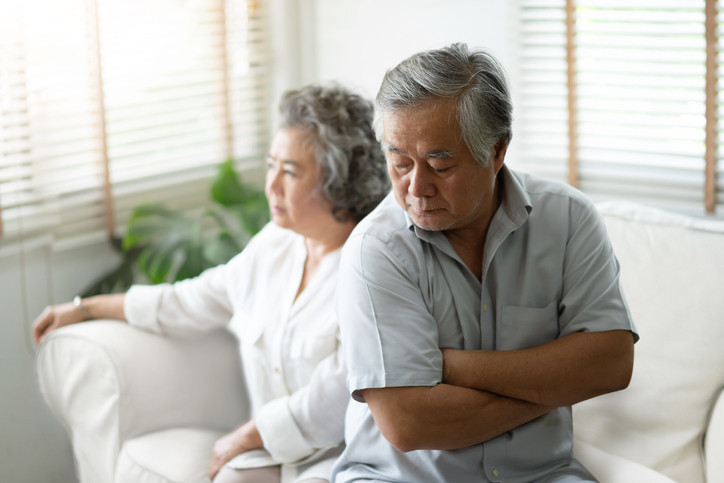 Upset couple sitting on a couch, woman looking ahead, man with crossed arms; concept is apology