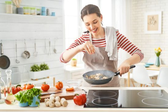 a woman smiles as she cooks mushrooms in a pan, demonstrating enjoyment and skill in a creative activity, highlighting the importance of engaging with one's talents for self-love.