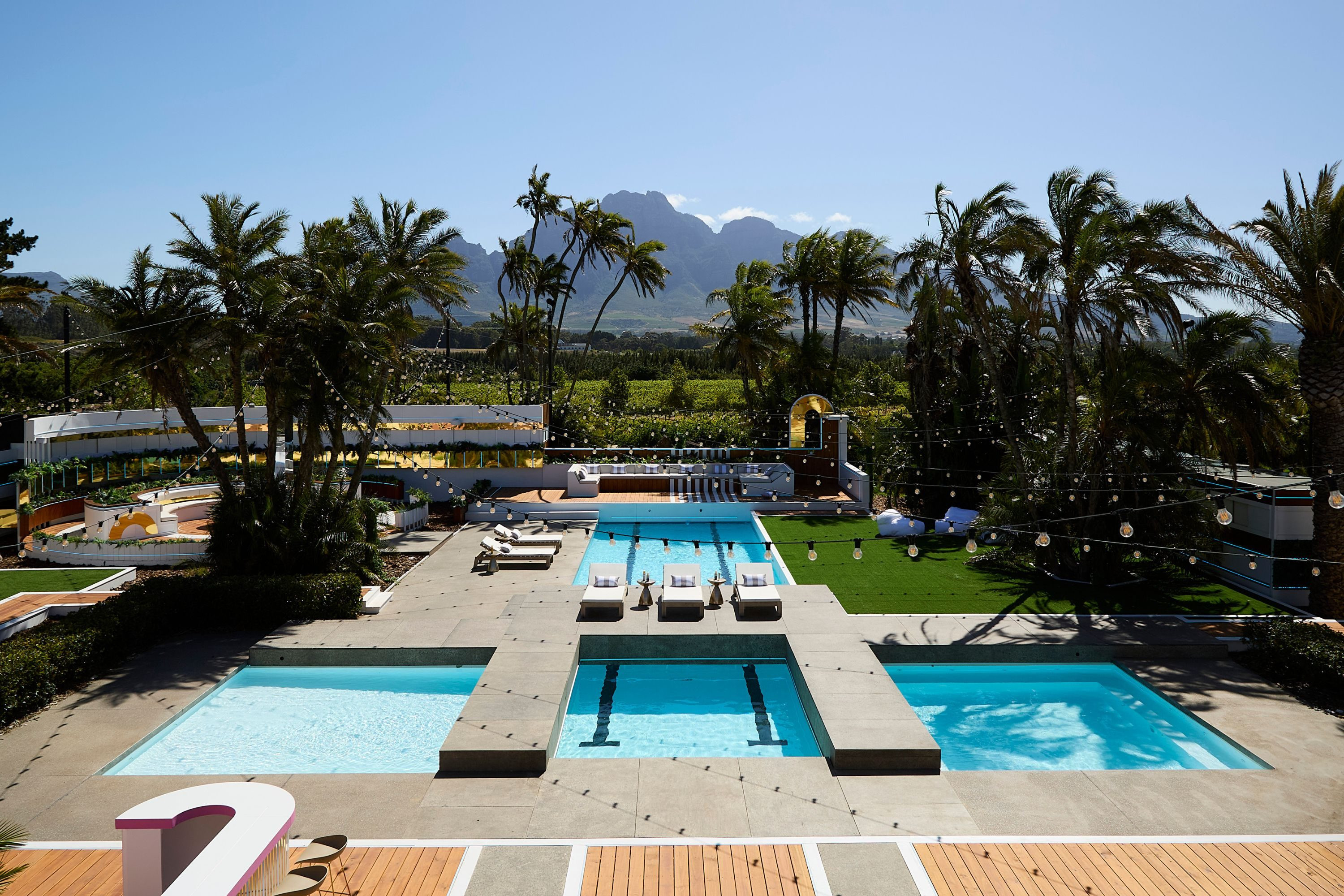 Aerial view of multiple swimming pools surrounded by palm trees and sun loungers.