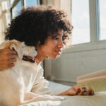 Woman reading Spanish romance novels with her pet dog on her bed.