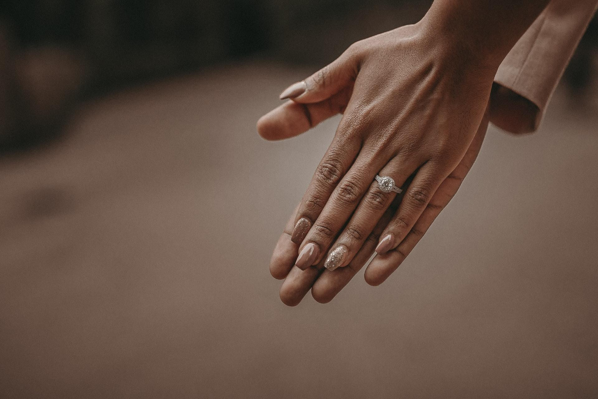 A couple holding hands with wedding rings visible, on a light yellow background.